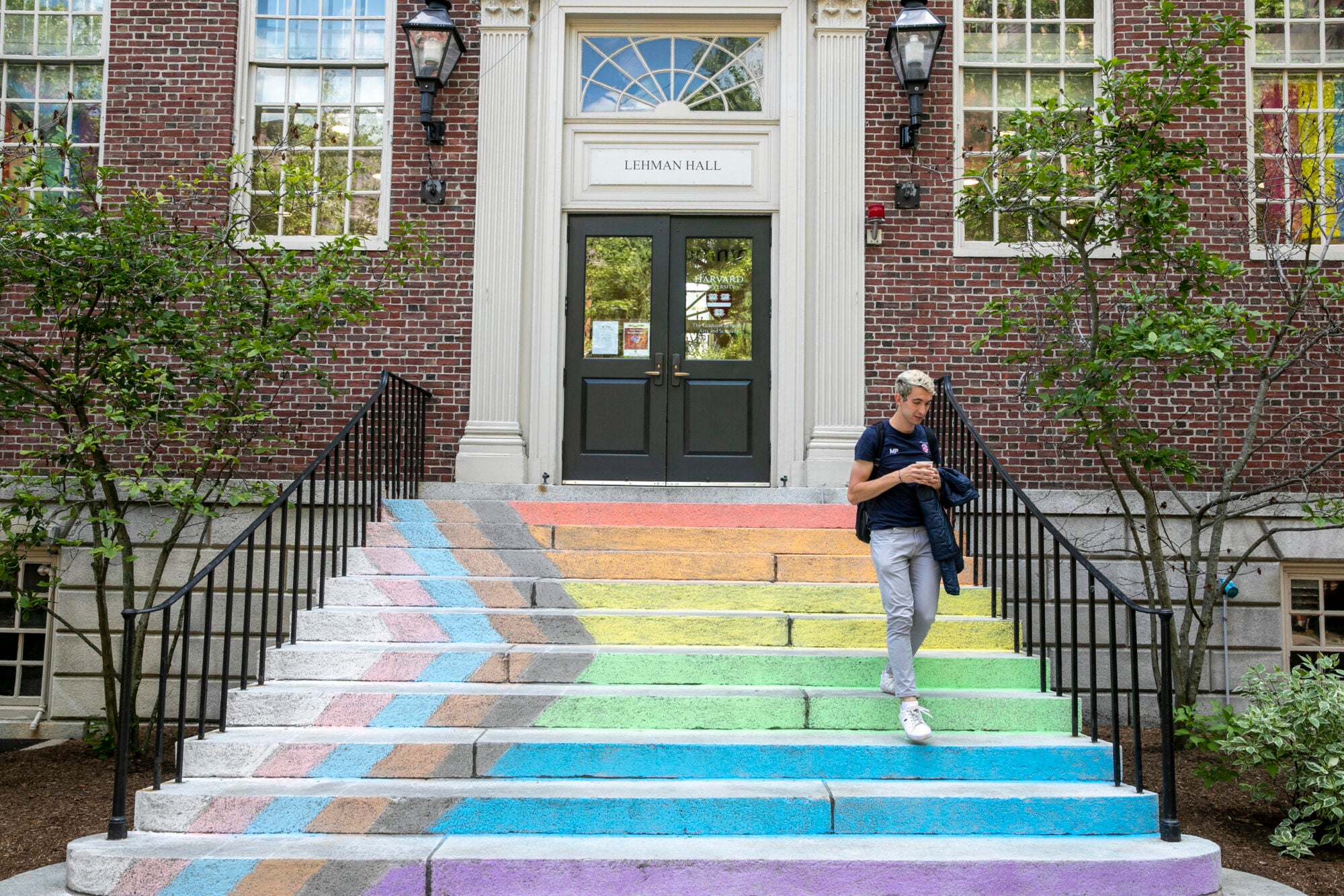 A student walks down a set of stairs that are decorated with chalk to represent the Pride flag