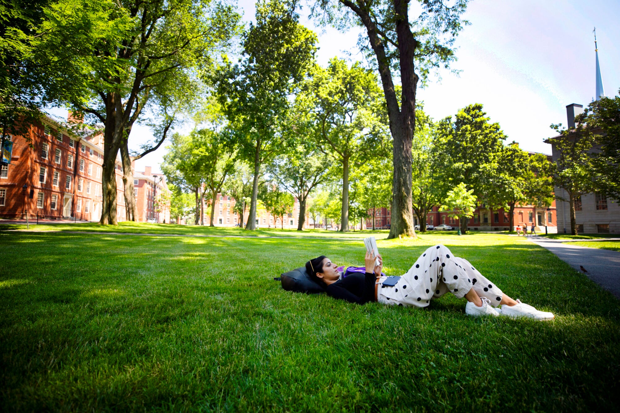 A young woman lays on grass reading a book
