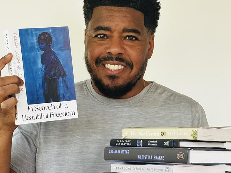 A man holds a stack of books on one hand and another book in the other