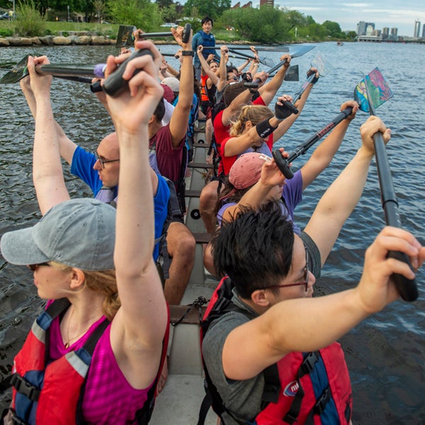 Members of dragon boat team raise their oars in the air while in the boat on the water