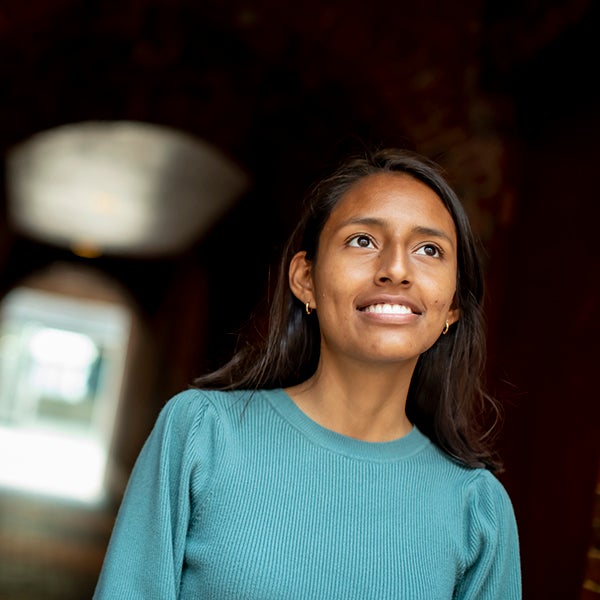 A young woman wearing a teal sweater looks upward