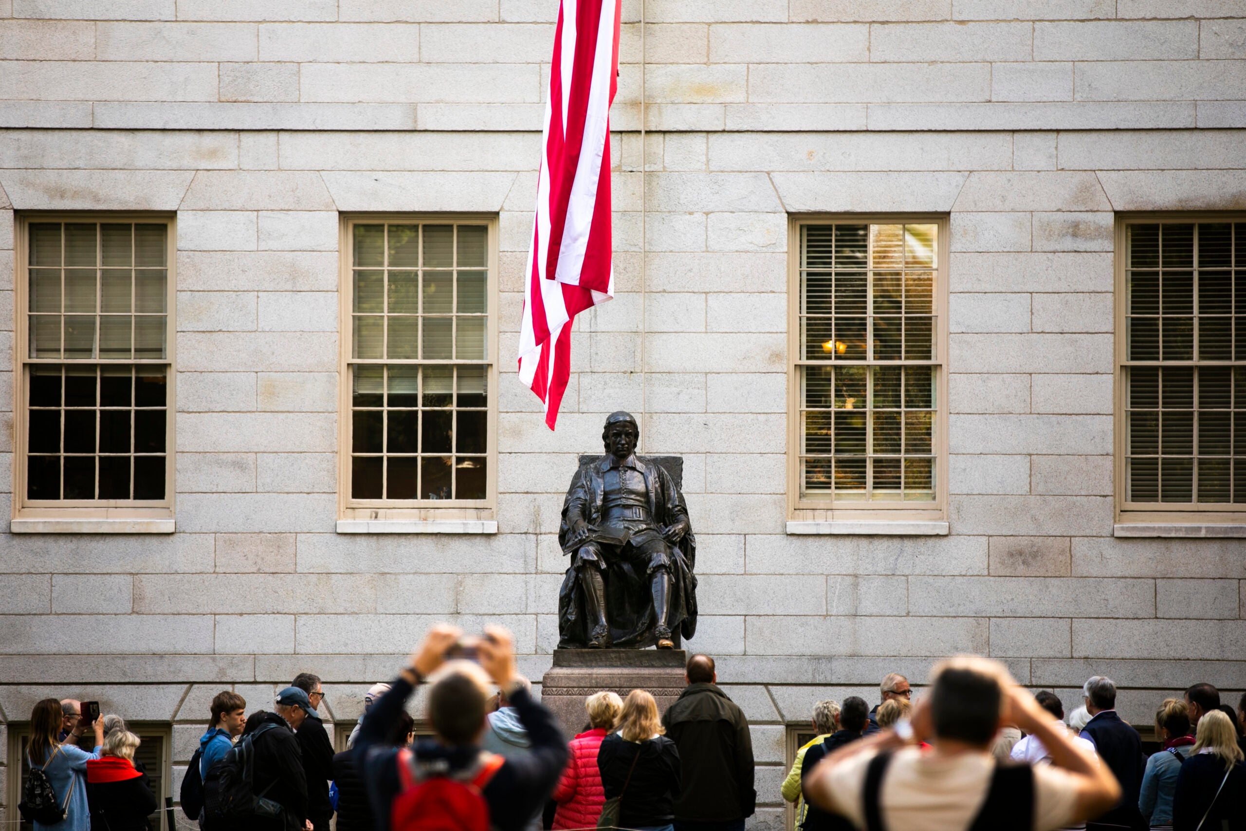 people taking photos of the John Harvard statue