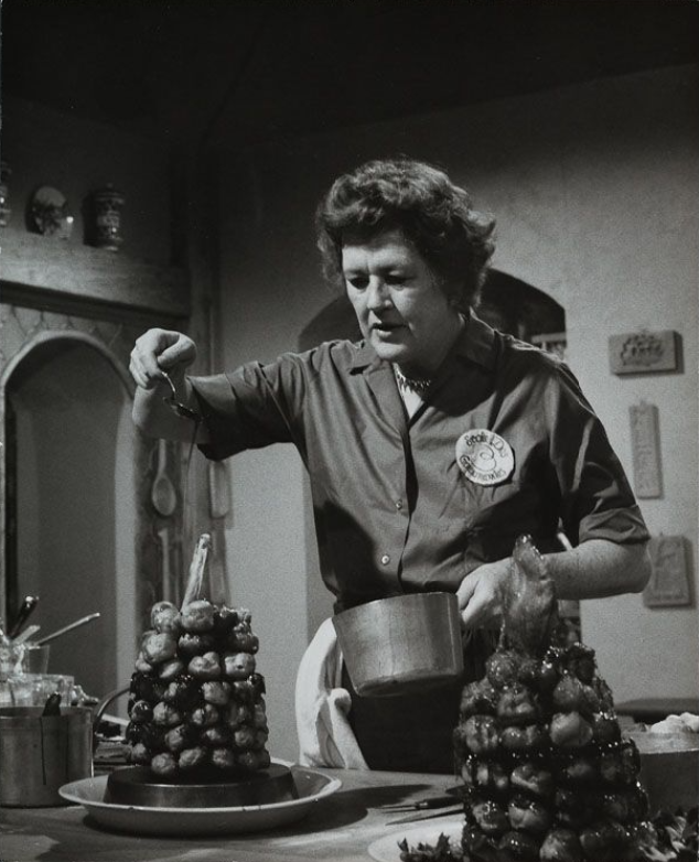 Julia Child pours hot syrup over a Croquembouche in a kitchen