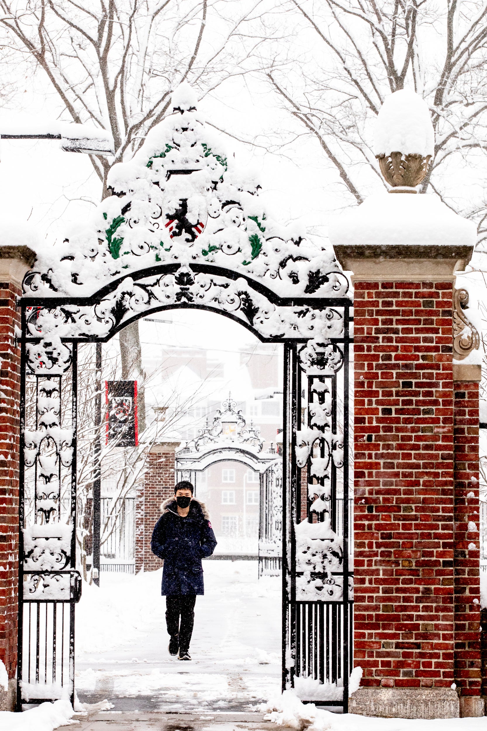 a student wearing winter weather gear walks through an iron gate