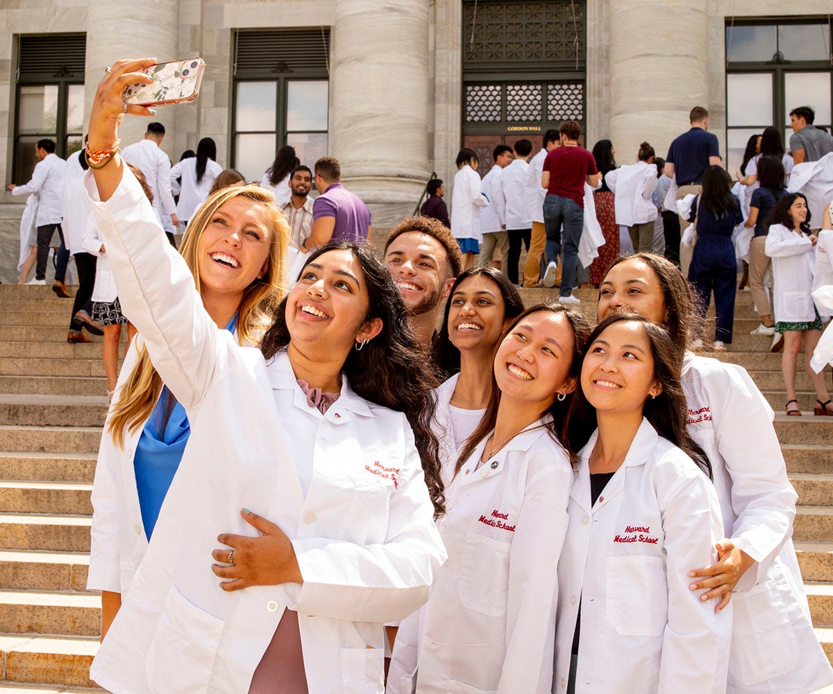 A group of students wearing white doctor's coats take a selfie together