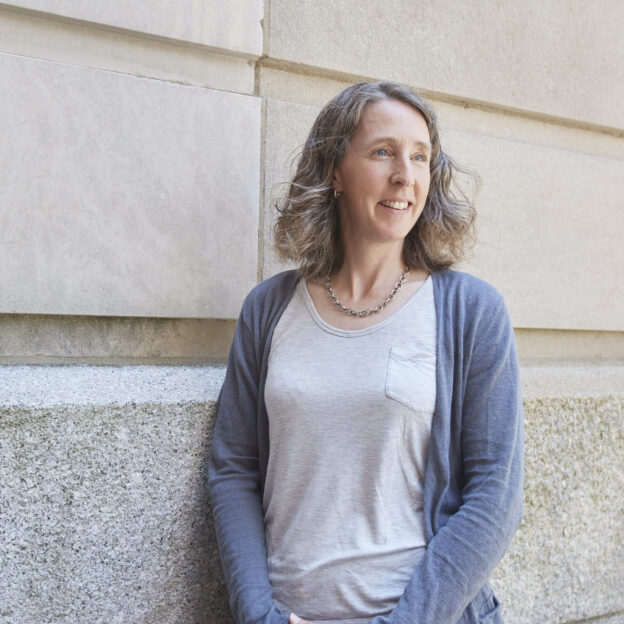 A woman stands outside, against a stone wall