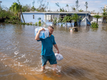 A man carries a package of bottled water through flood waters
