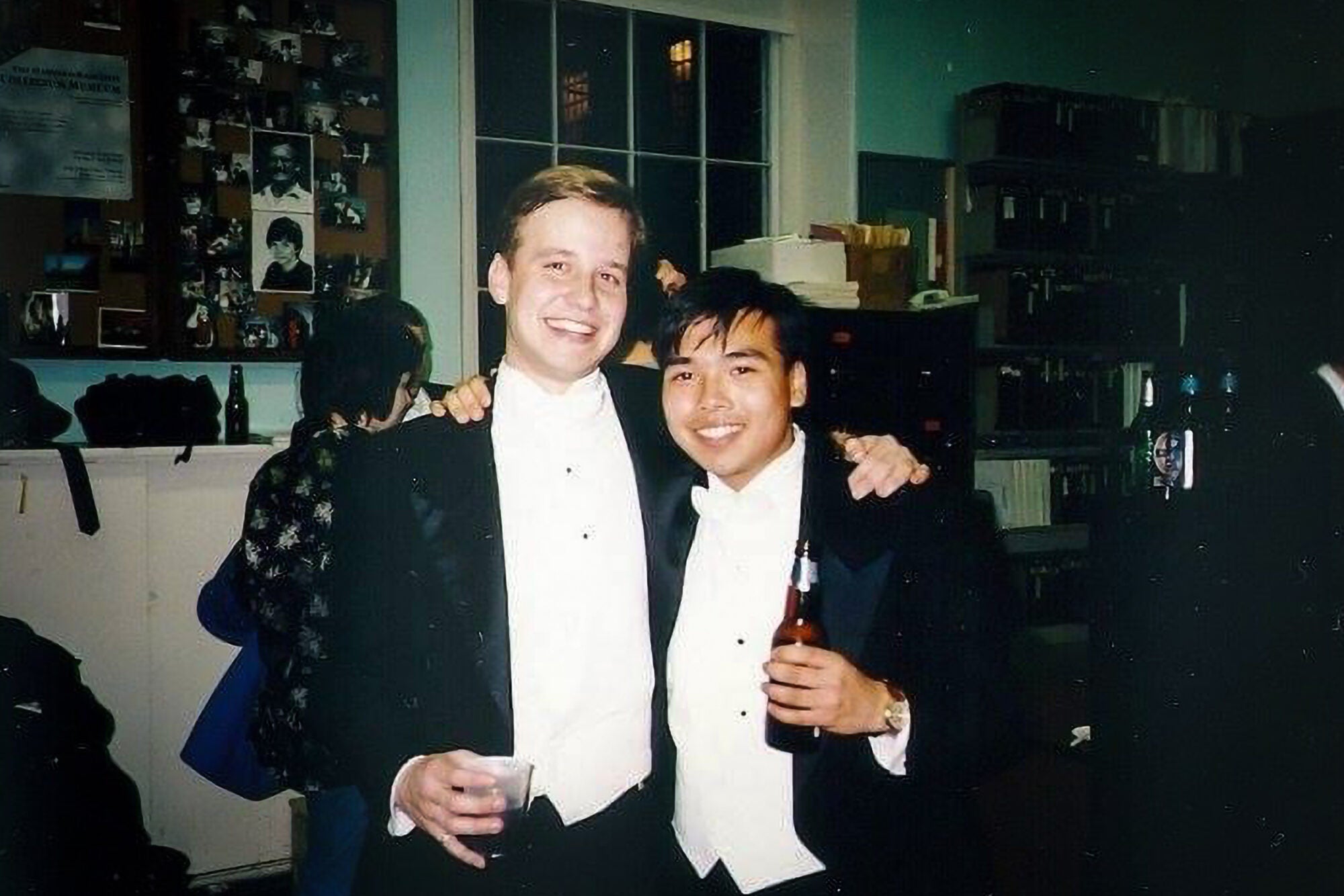 Two men wearing tuxedos pose for a photo