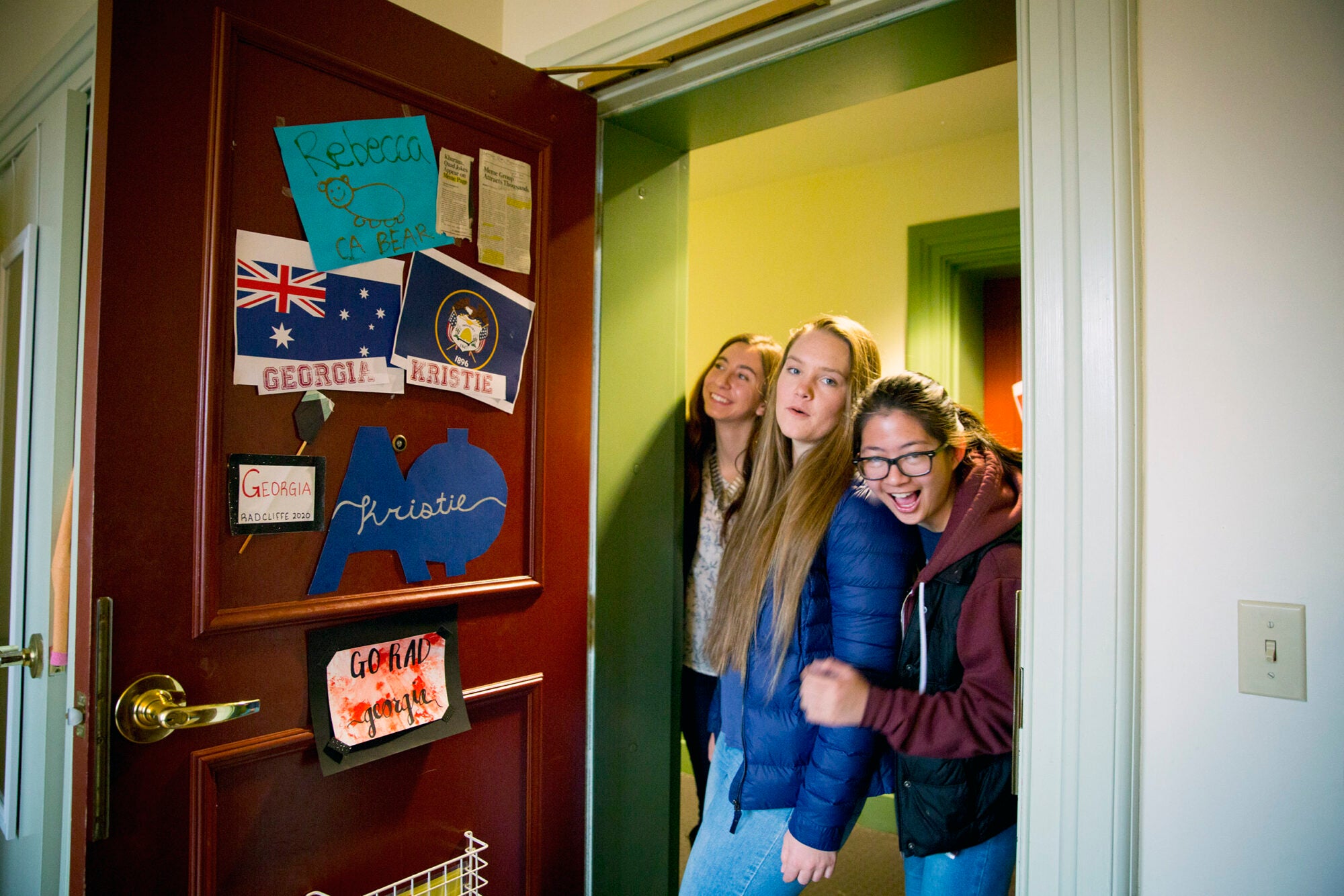 Three young women roommates stand in the doorway of a dorm room