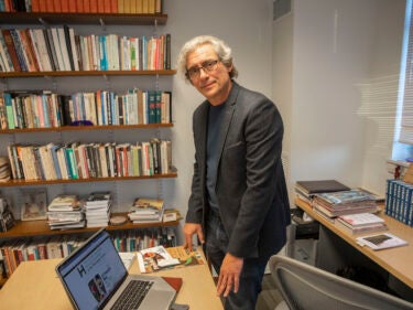 A man stands in his office with a desk and books around him