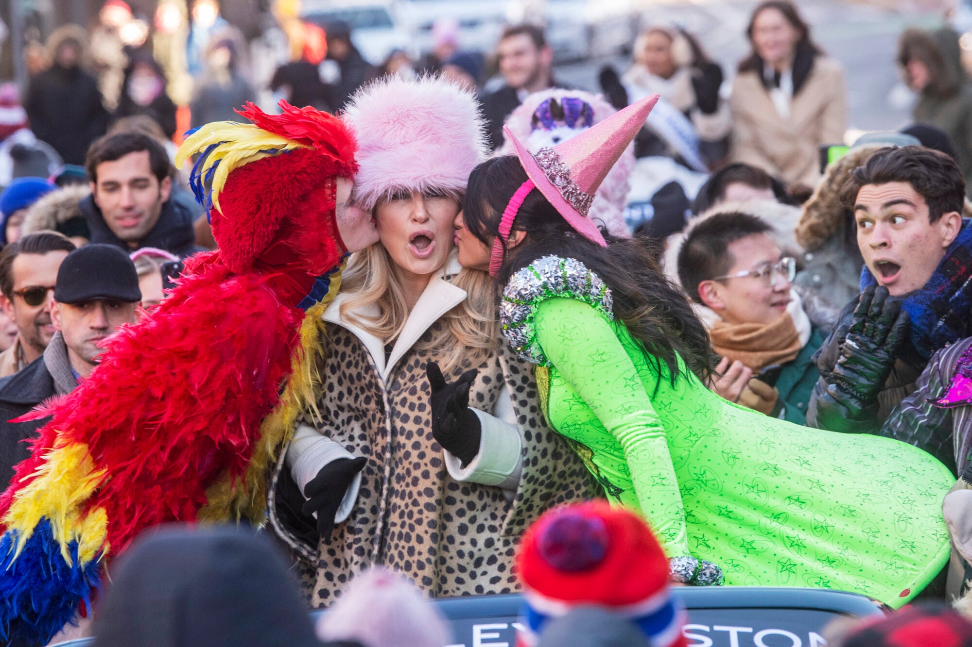 Jennifer Coolidge gets a kiss on each cheek from students wearing costumes during a parade