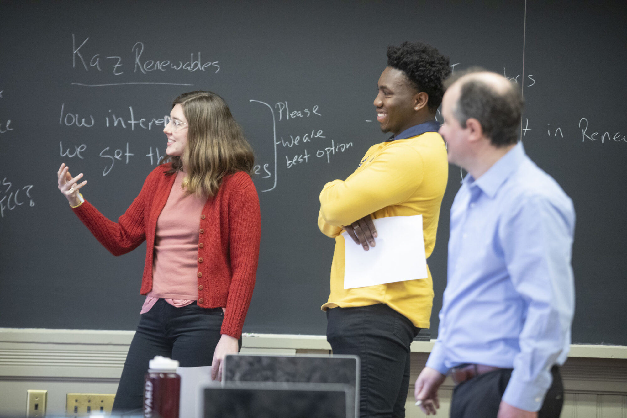 Two students and a faculty member stand in front of a chalkboard