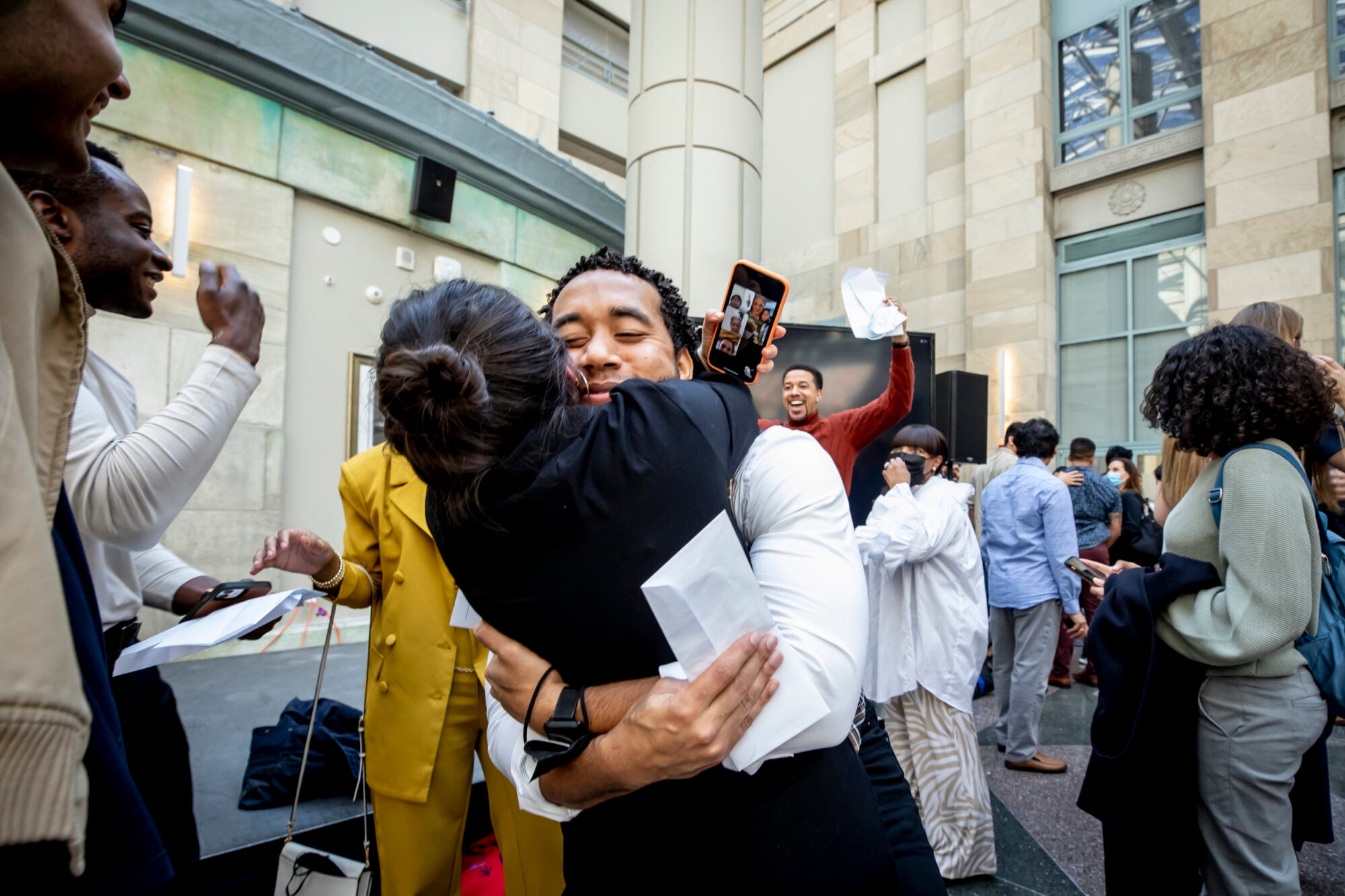 Two students hug while others celebrate in the background