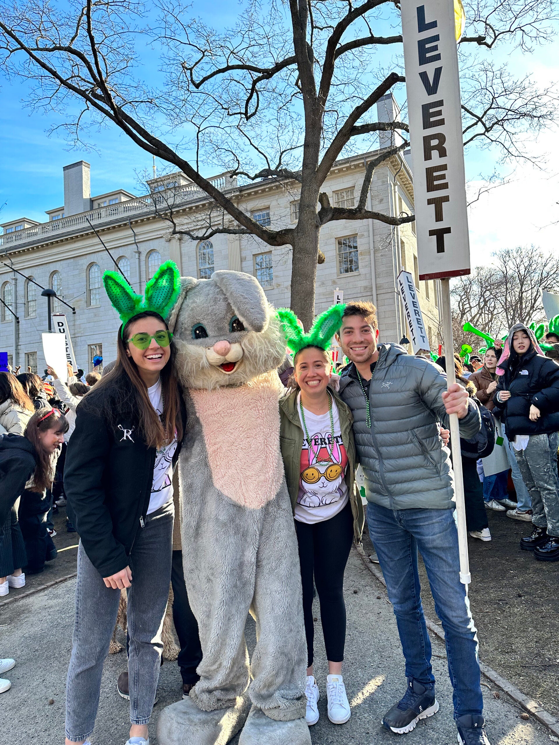 Three students stand with a student in a rabbit costume. Two students wear green bunny ears and one holds a Leverett sign