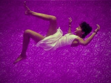 A woman floats in a dream-like state against a purple backdrop