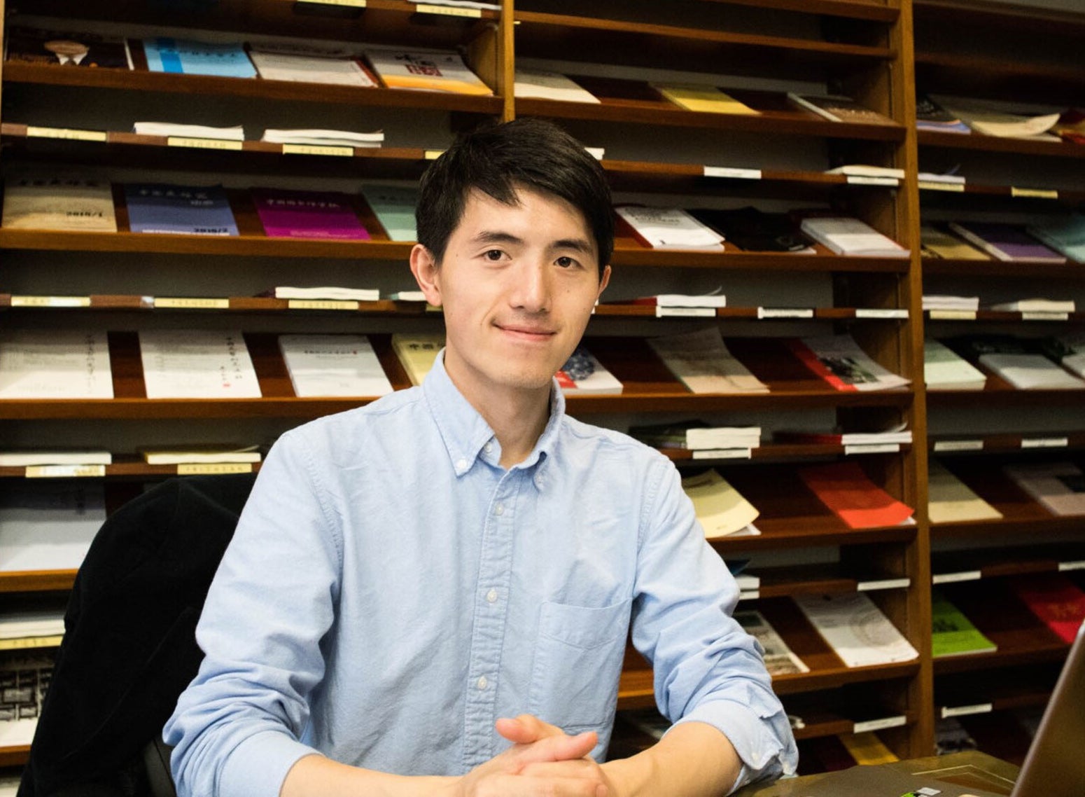 A young man sits in front of large book shelves containing research and other materials