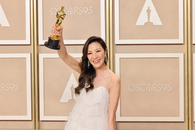 Michelle Yeoh holds her Academy Award in front of an Oscars step-and-repeat while wearing a beautiful blush gown
