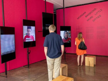 Videos from the “Quarantunes” series play on multiple screens as people walk around the exhibit.