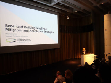 A person at a podium next to a screen with a presentation