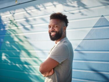 Baratunde Thurston smiles and stands with his arms crossed