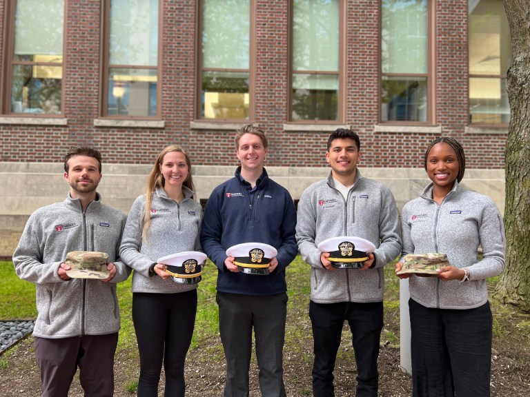 Five students pose together holding the caps representing the military branches they plan to join.