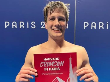 A swimmer holds a "Harvard Crimson in Paris" Olympics sign.