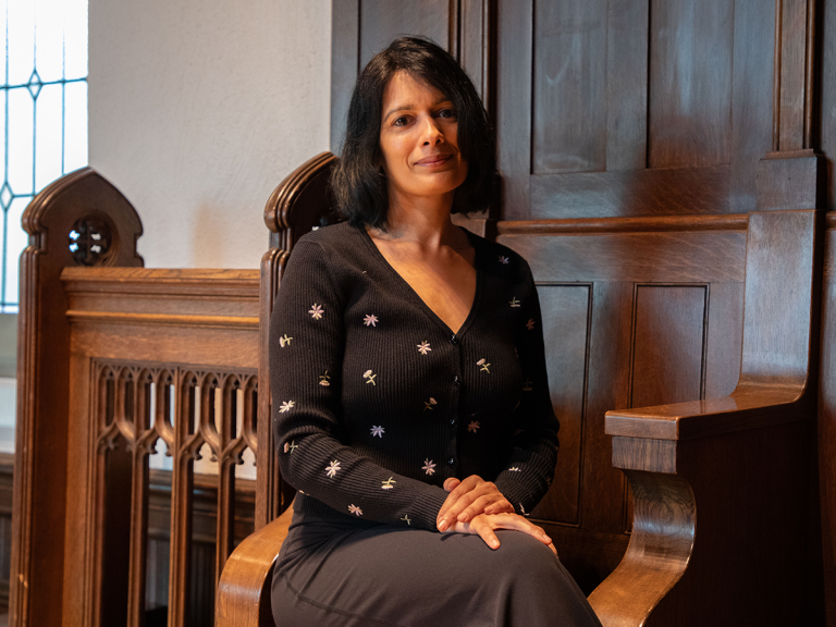 Sabbi Lall sits in a wodden pew.