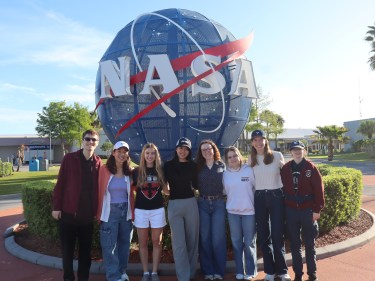 Students stand in front of the NASA logo at the Kennedy Space Center