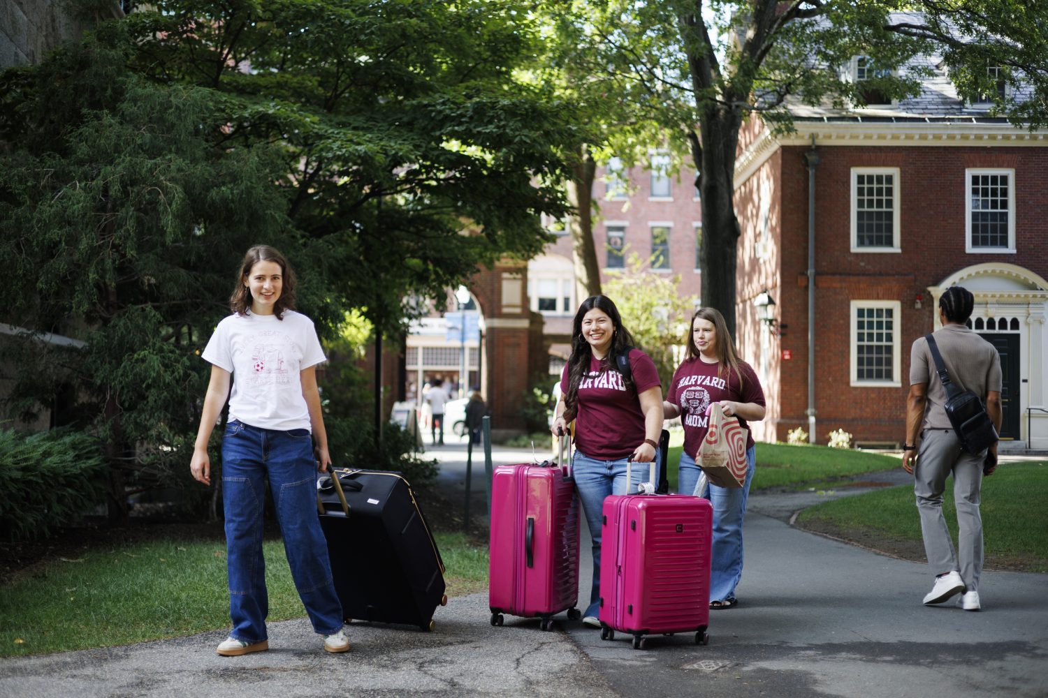 Three students wheel suitcases across campus.