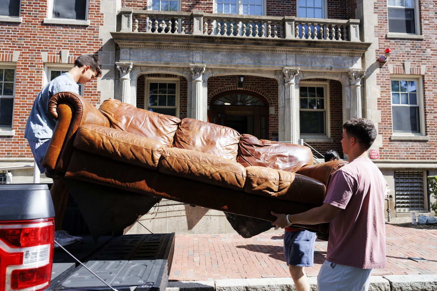 Two people move a couch out of the back of a truck.